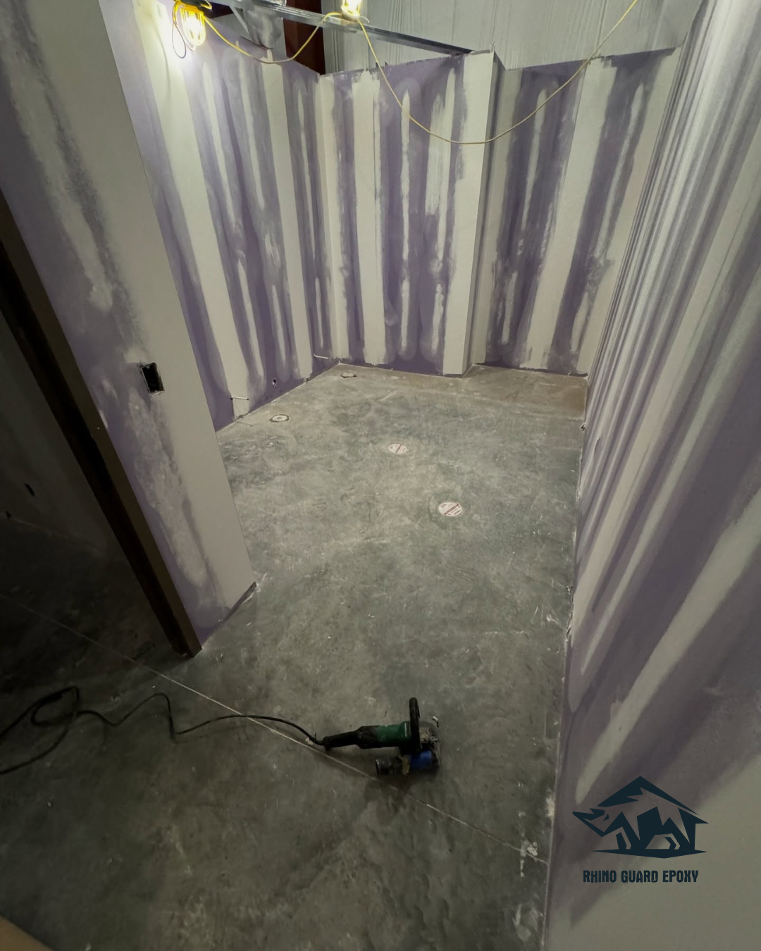 Unfinished utility room under construction with taped drywall, hanging wires, and a power tool on a concrete floor.