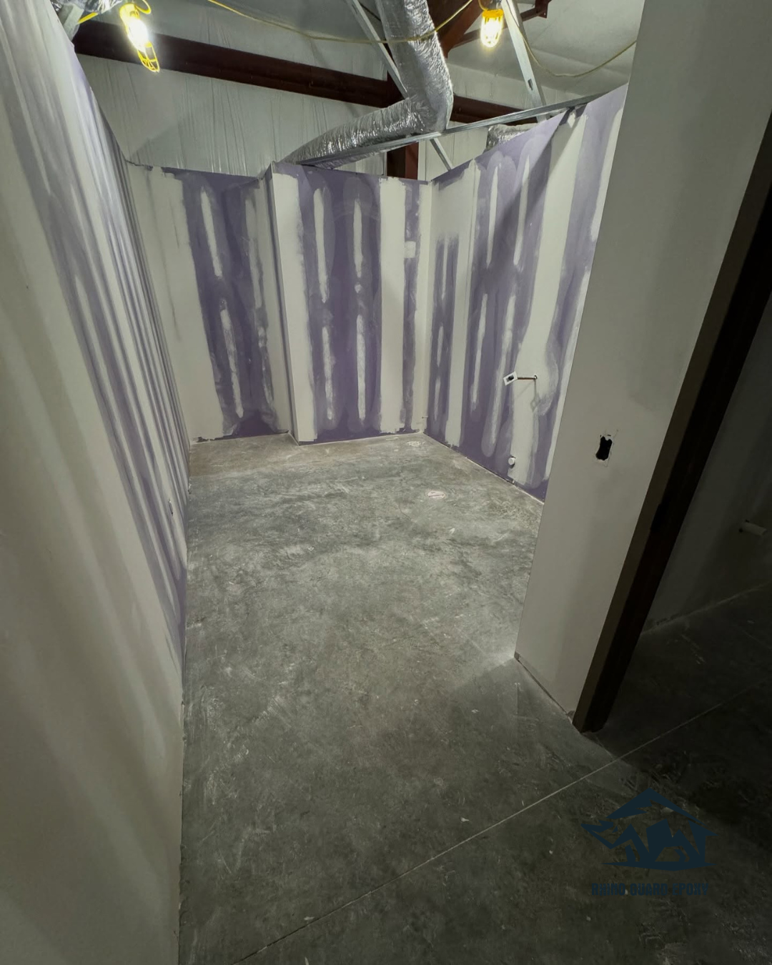 Narrow unfinished room under construction with purple drywall panels and exposed ducts overhead.