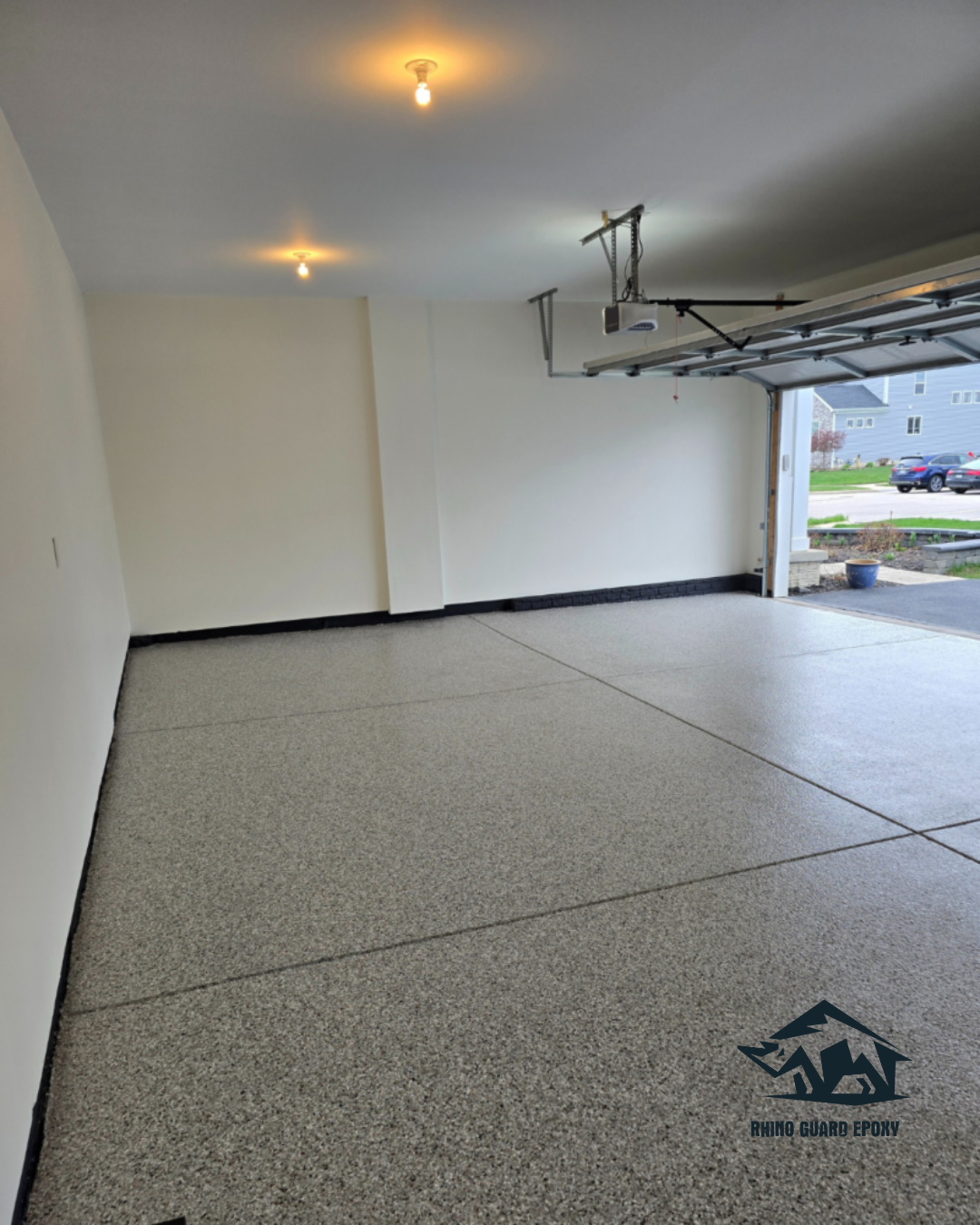 Clean two-car garage with speckled epoxy floor, white walls, and an open garage door showing a neighborhood street.